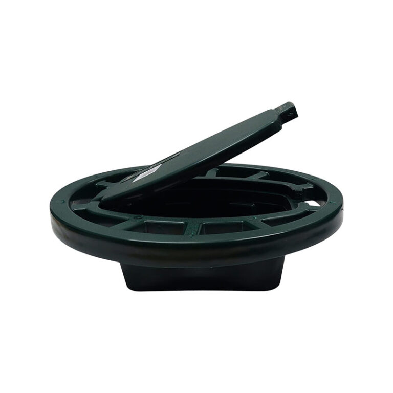 Green circular manhole/access cover with a rectangular lifting tool resting on its edge.