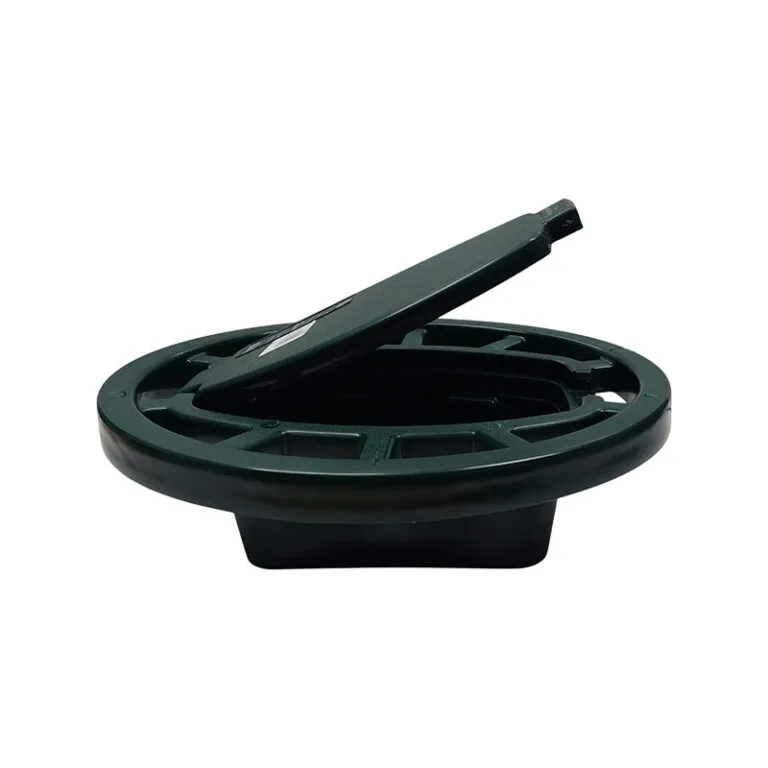 Green circular manhole/access cover with a rectangular lifting tool resting on its edge.