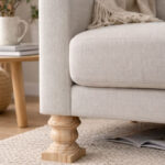 Close up of a Beige Upholstered Sofa with a Carved Wooden Leg on a Woven Rug in a Cozy Living Room