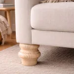 Close up of a Light Wood Turned Sofa Leg Supporting a Beige Fabric Couch on a Textured Rug