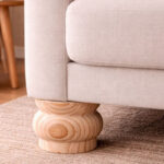 Untitled-1 | Securadeal Close up of a Beige Upholstered Sofa with a Rounded Turned Wooden Leg Sitting on a Light Brown Rug