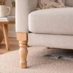 Untitled-1 | Securadeal Beige Upholstered Sofa with a Wooden Leg on a Light Rug a Magazine is Tucked Beneath the Seat
