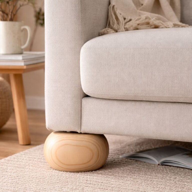 Beige upholstered sofa with a rounded wooden foot on a light rug in a cozy living room.