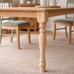 Untitled-1 | Securadeal Close up of a Carved Wooden Table Leg in a Light Wood Dining Table with Chairs and a Woven Rug in the Background