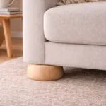 Close up of a Light Beige Fabric Sofa with a Rounded Wooden Foot Resting on a Beige Carpet