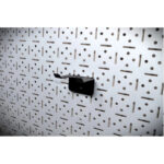 2 | Securadeal Black Wall mounted Hook Attached to a Perforated Metal Panel with Repeated Holes and Slits in an Industrial Setting