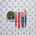 2 | Securadeal Yellow and black Stanley Tape Measure and Five Colored Markers Arranged Horizontally on a Grey Perforated Pegboard Wall