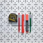 2 | Securadeal Yellow and black Stanley Tape Measure and Five Colored Markers Arranged Horizontally on a Grey Perforated Pegboard Wall