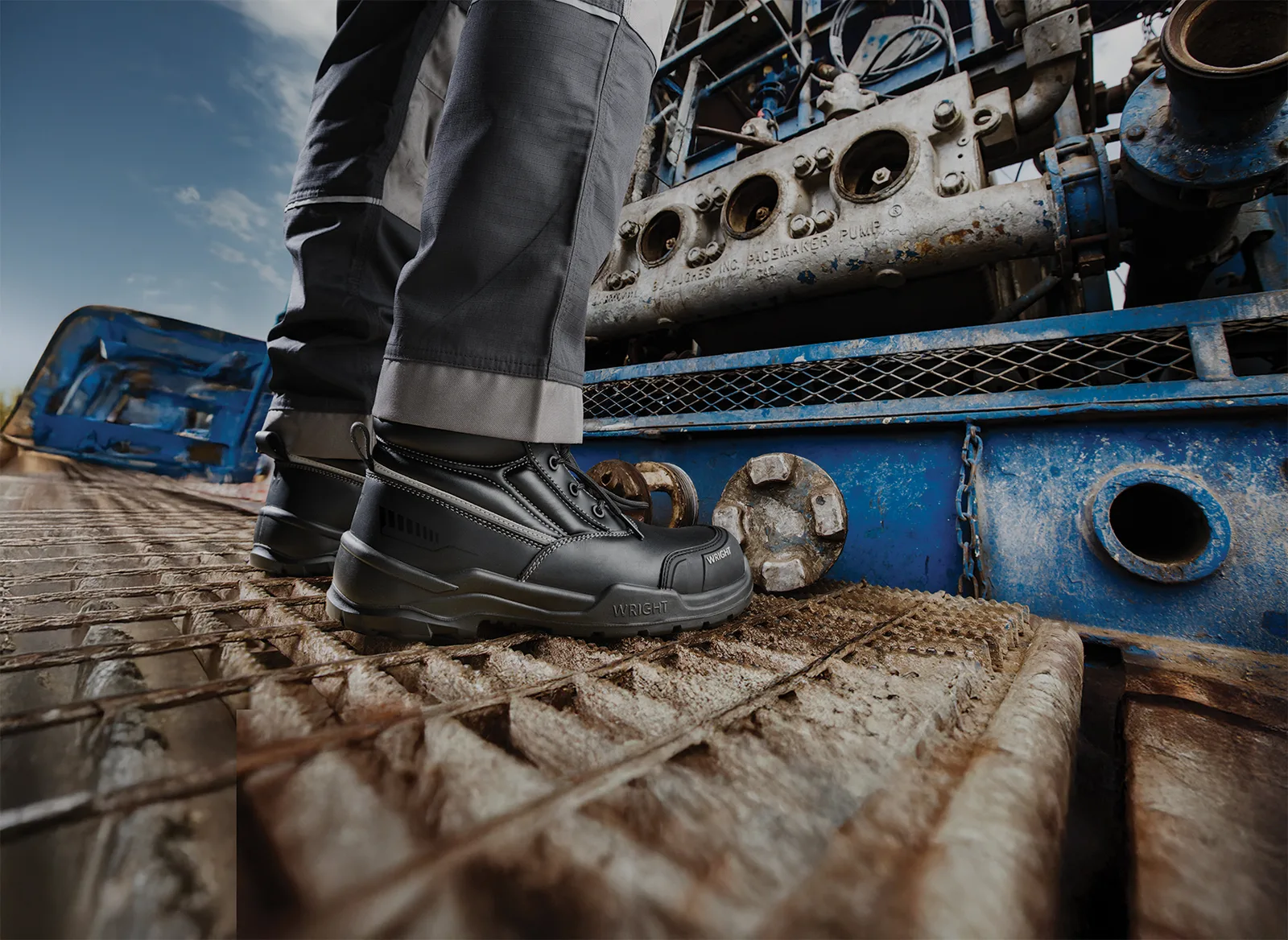 Close up of a Workers Black Safety Boots on a Rusty Metal Platform Beside Blue Industrial Machinery