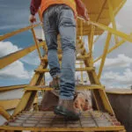 Wright-Onyx-Lifestyle | Securadeal Construction Worker in an Orange Safety Vest Climbs a Yellow Metal Staircase on an Outdoor Site