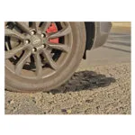 2 | Securadeal Car Wheel with Alloy Rim and Red Brake Caliper Resting on a Gravel Surface Beside a Paved Road